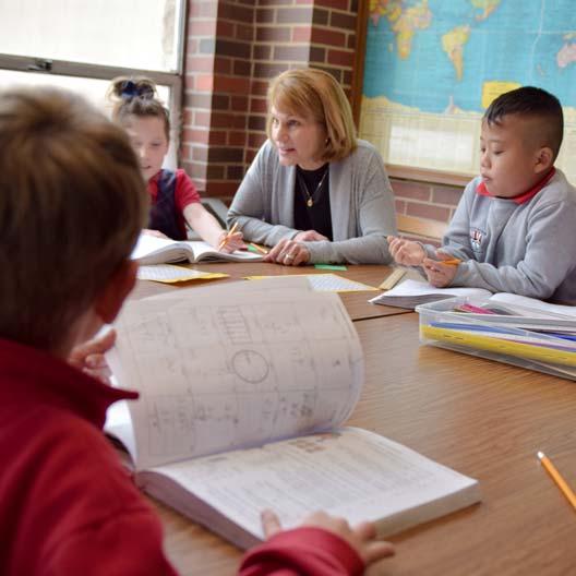 A teacher sits with young students at a table