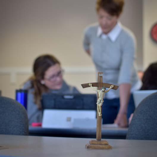 A Crucifix in the foreground with a student and graduate and teacher in the background